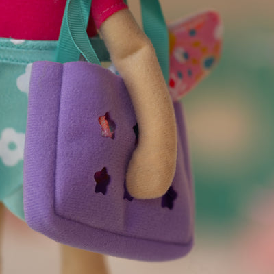 close up of a soft doll holding a purple bag with a pink floral towel inside it.