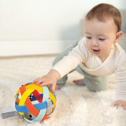 Baby reaching for a colorful textured sensory ball while playing on a soft white rug.