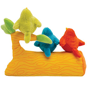 Back view of three plush birds, green, blue, and red, sitting on a plush orange tree branch toy with green leaves.