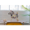 Decorative zebra plush toy with colorful stitched accents displayed on a bench in a bright, modern room.