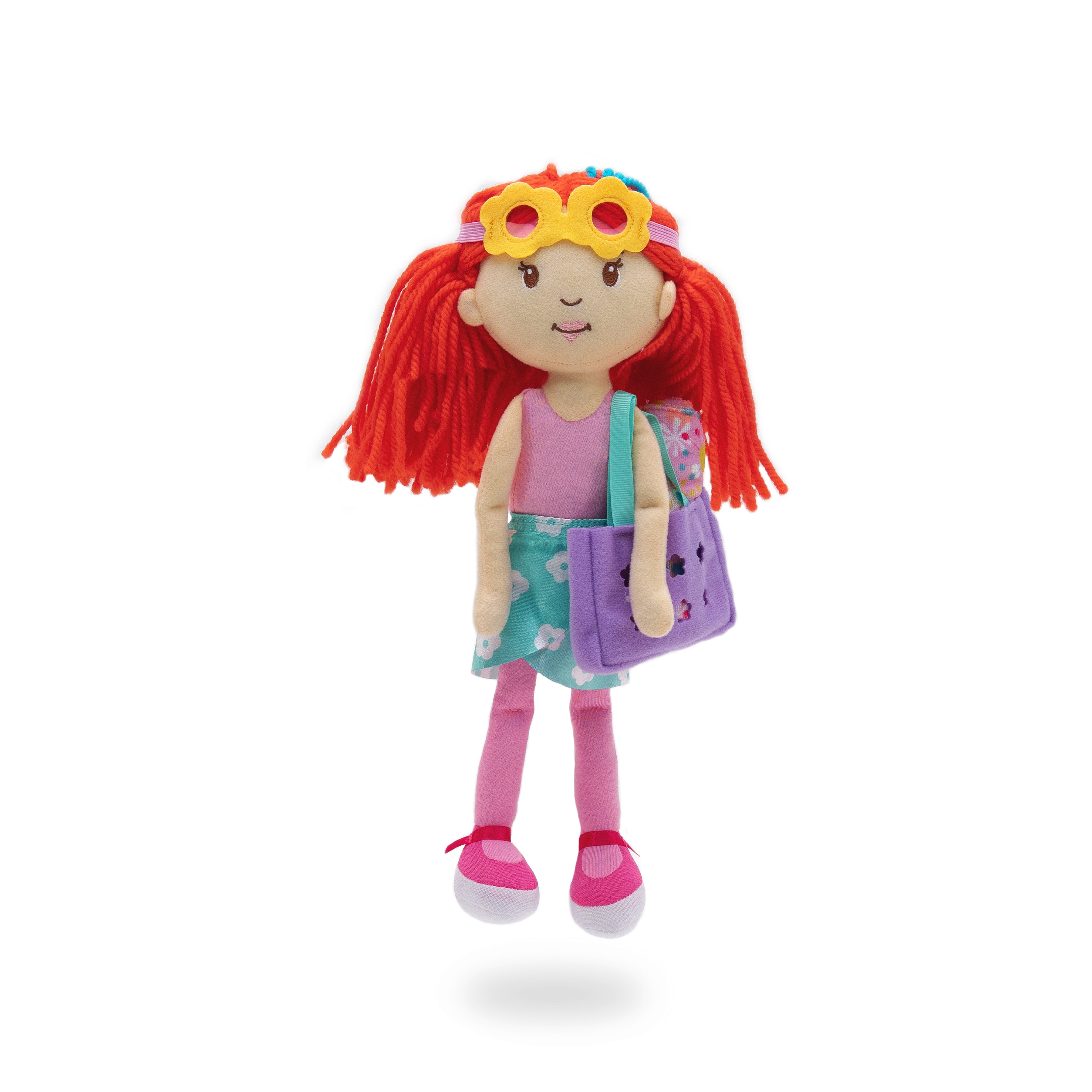 Soft doll wearing blue floral wrap skirt and flower goggles with a floral towel in a purple bag.