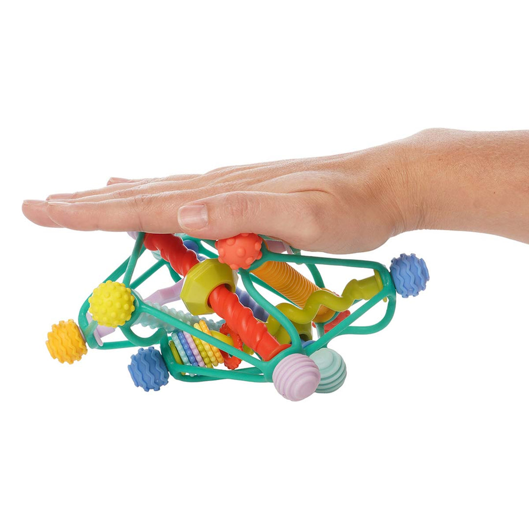 A hand pushes down on the colorful Whirzle infant toy, squishing it to show its flexibility.