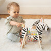 Toddler playing with a plush zebra activity toy on a soft white rug.