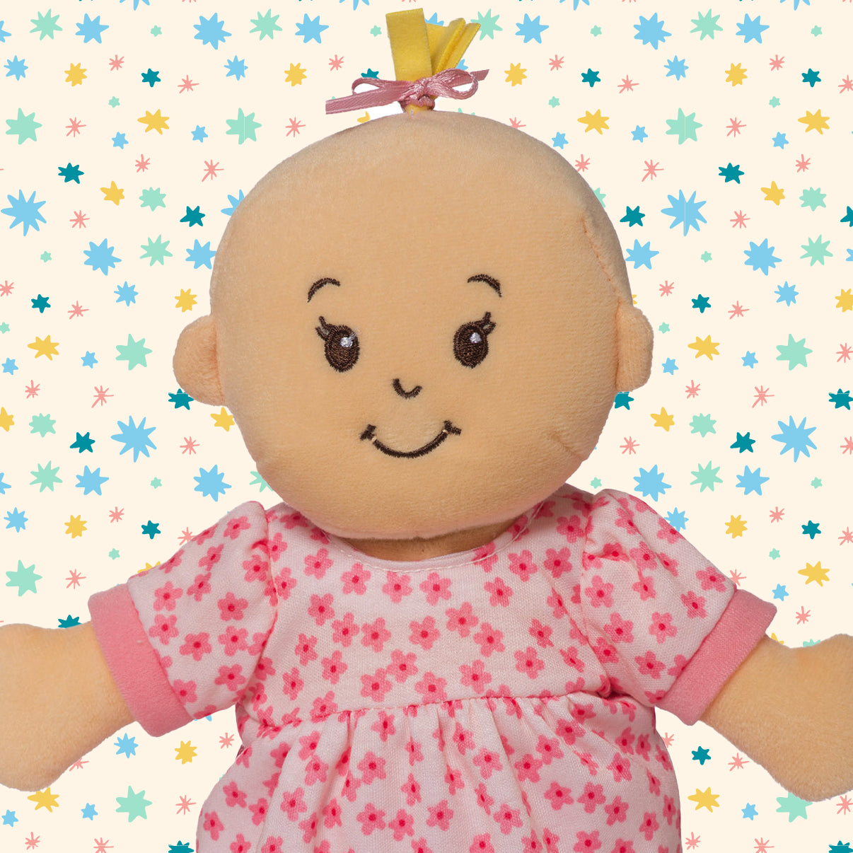 Stella doll with blonde hair, wearing a pink dress, sitting on a pattern background.