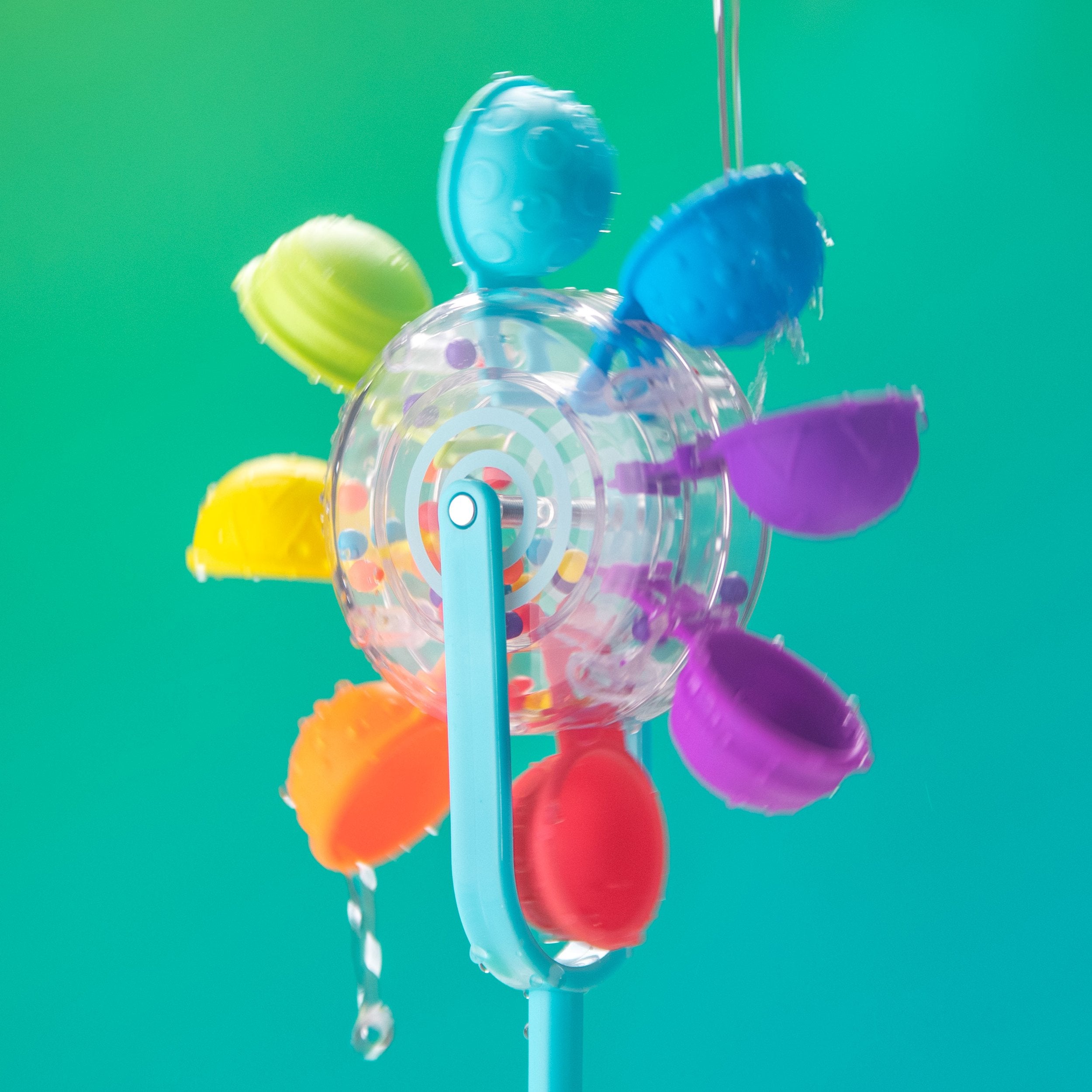 Colorful water toy with spinning rainbow cups being powered by falling water, set against a blue and teal background. Static Image